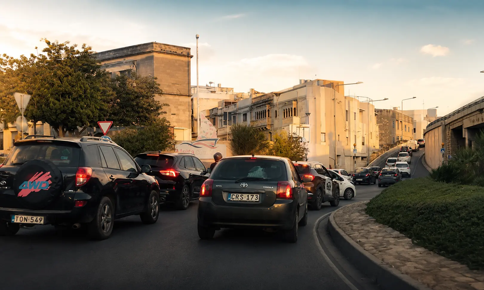 Traffic and driving conditions in Malta during afternoon rush hour near a roundabout between residential urban areas.