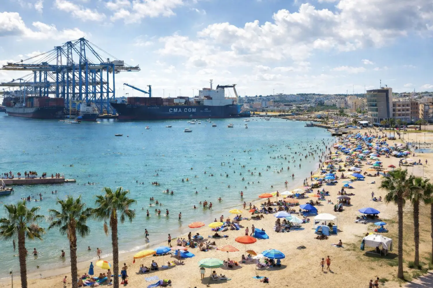 Birżebbuġa Pretty Bay beach with people swimming and Malta Freeport container port in the background